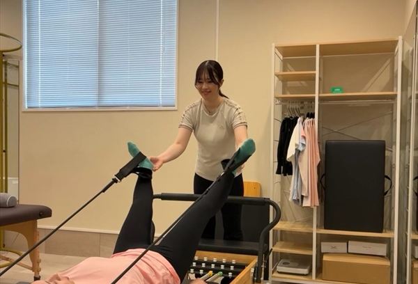 リフォーマーでの脚のエクササイズをサポートするインストラクター